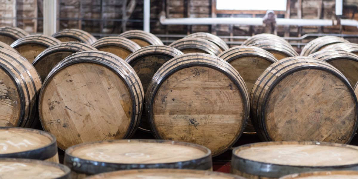 Stacks of wooden bourbon barrels in a distillery warehouse.