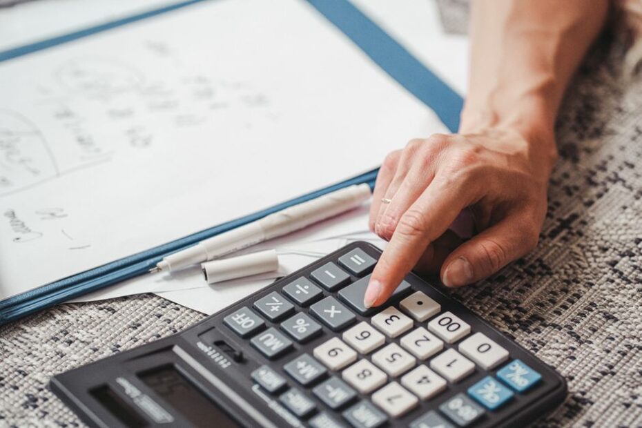 Person sits at a clean, modern desk, using a calculator while carefully reviewing a stack of papers related to a home sale...