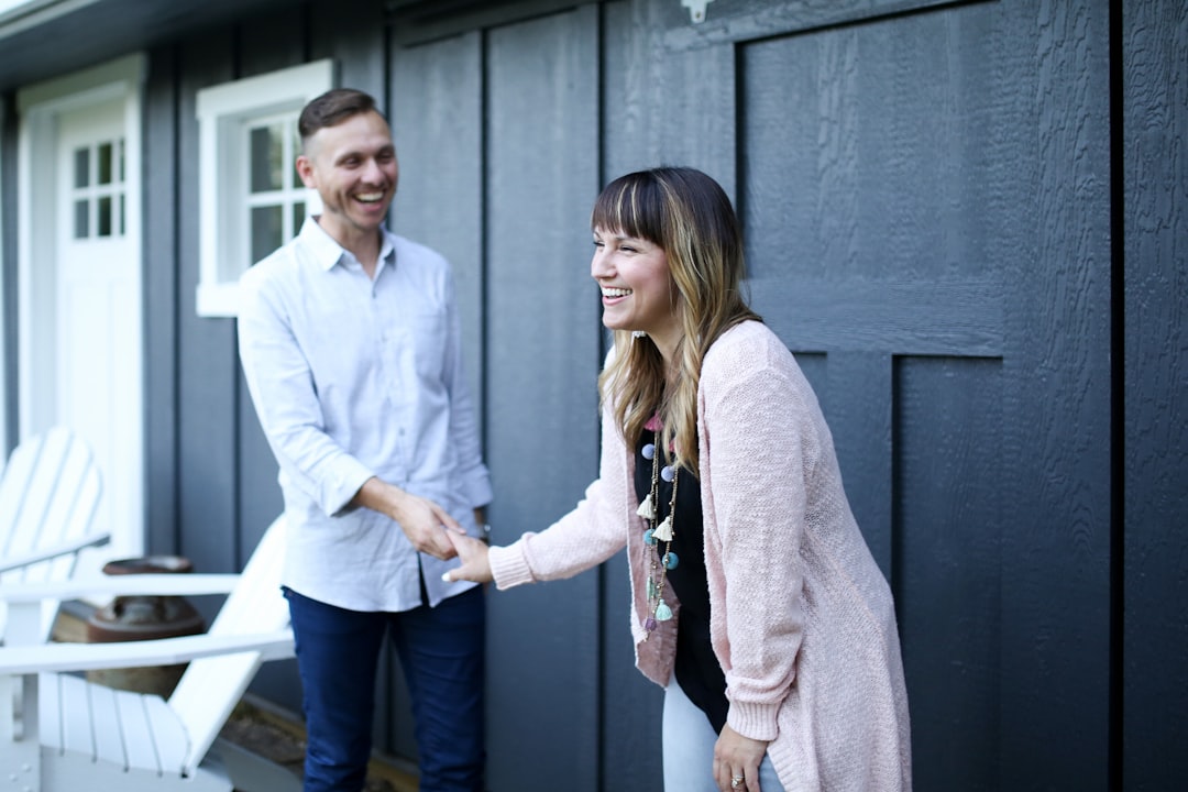 A professional couple sits at a modern wooden table, carefully signing the final closing documents for their home sale with a pen.