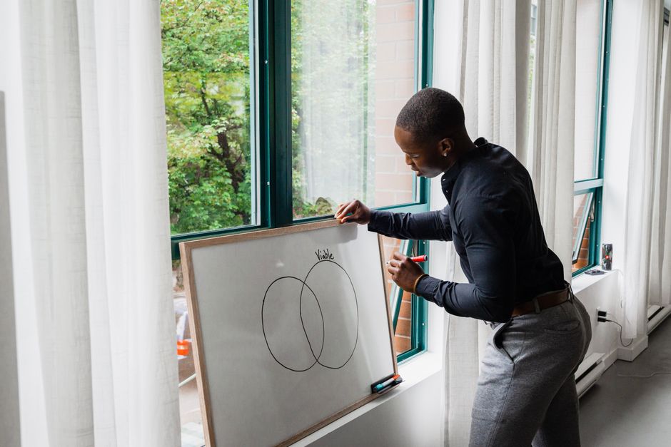 A technology professional in a bright, modern office sketching a complex systems diagram on a glass wall, illustrating the CTO's role in comparing frameworks.